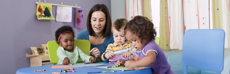 Teacher and three small children sitting at a table coloring