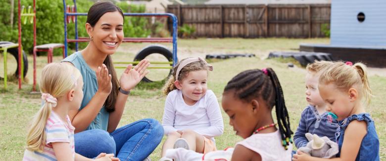 A female preschool teacher playing outside with four young girls.
